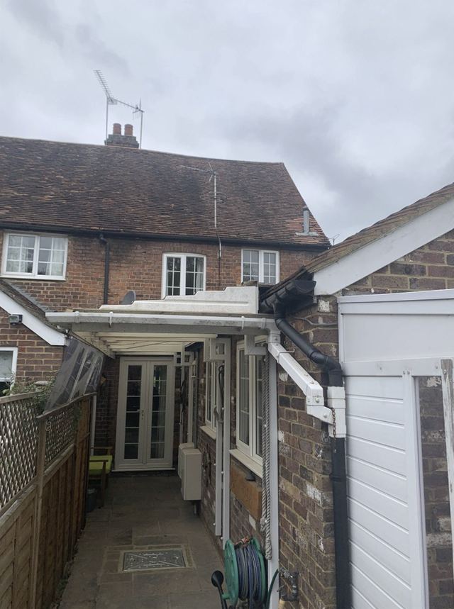 A narrow unused side passage between the house and an outbuilding, covered by a translucent canopy