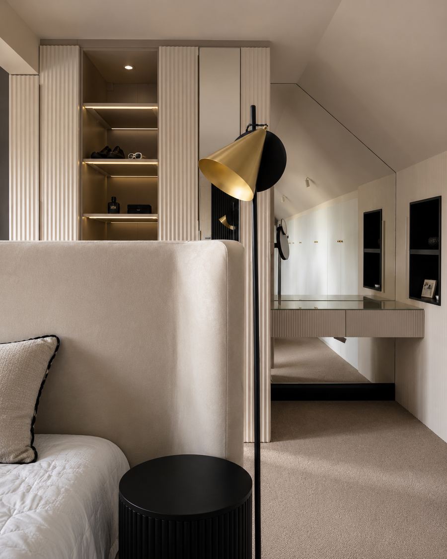 The completed dressing area beside the bed, with fluted joinery, lit open shelving, a mirrored wall and a vanity