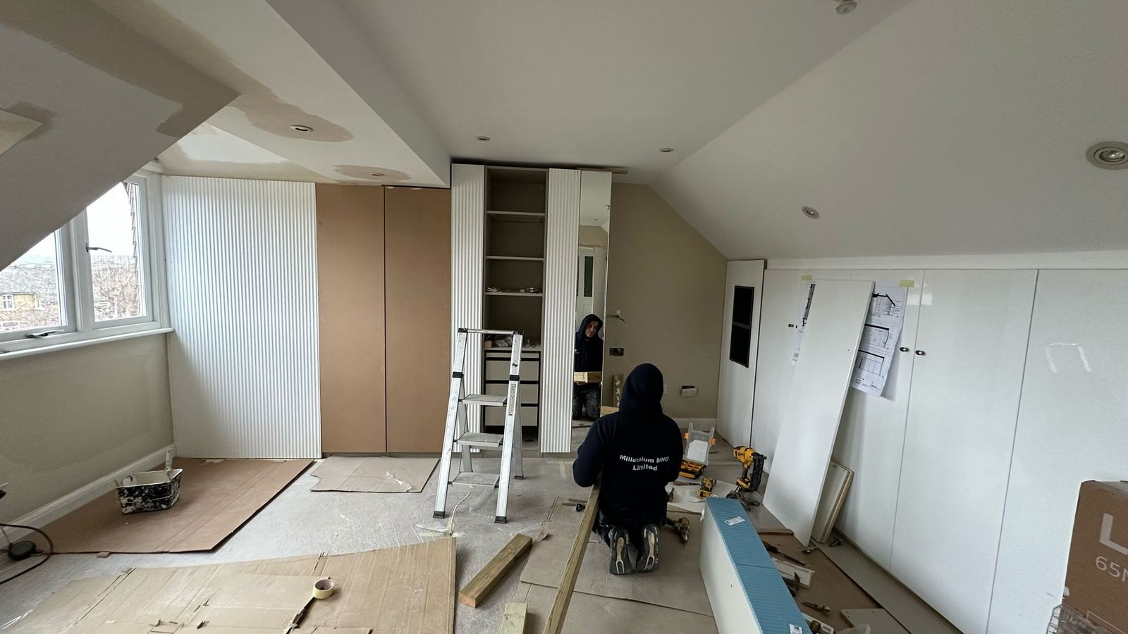 Joinery being installed in the attic bedroom, with drawings taped to the wardrobe doors